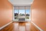 Room featuring a large window with urban scenery, wood-finish flooring, and light-toned walls