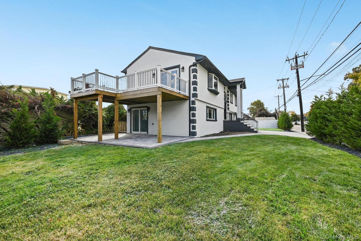 Back of property featuring stucco siding, a patio area, a lawn, and a deck