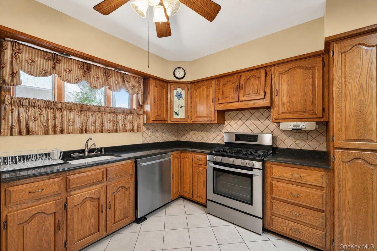 Kitchen featuring solid wood cabinetry, black countertops, a stainless steel range, stainless steel dishwasher, and a white tile floor