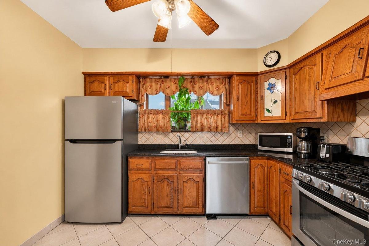 Kitchen featuring wood cabinetry, stainless steel appliances, dark countertops, and a tiled backsplash