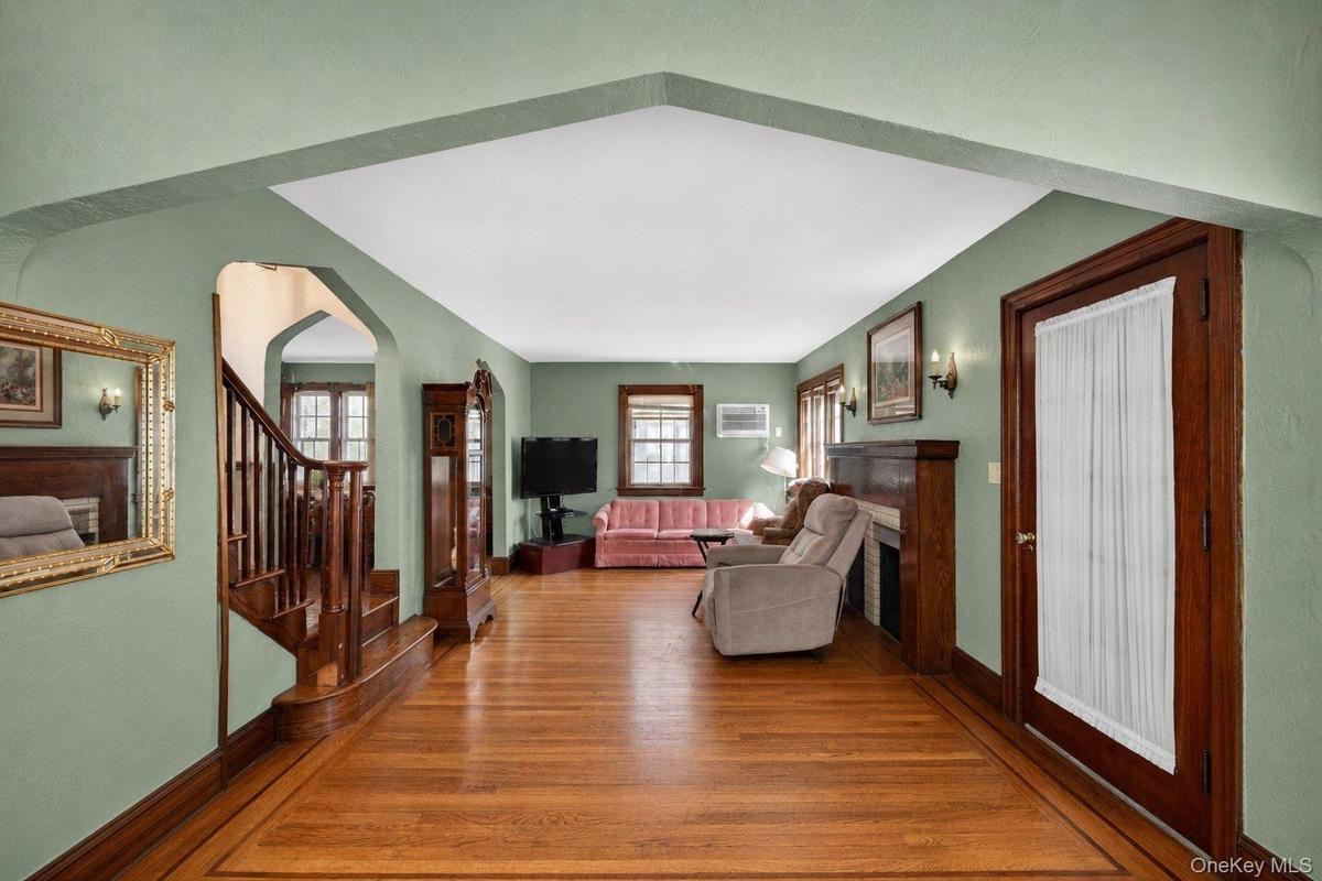Hardwood flooring with a decorative border, featuring a staircase with wood railing and an arched entryway