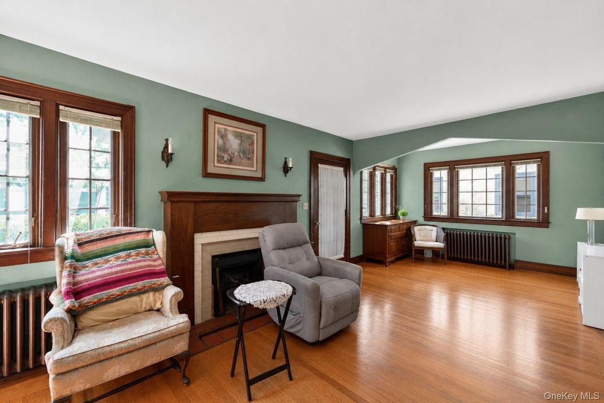 Spacious living area featuring hardwood flooring, a prominent fireplace with a wood mantel, and multiple windows with dark wood trim