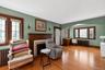 Spacious living area featuring hardwood flooring, a prominent fireplace with a wood mantel, and multiple windows with dark wood trim