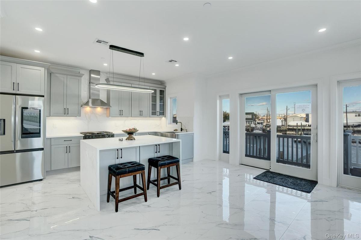 Kitchen featuring stainless steel refrigerator with ice dispenser, glass insert cabinets, a kitchen island, light marble finish flooring, and a breakf