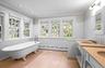 Bathroom featuring a wainscoted wall, a freestanding tub, baseboard heating, crown molding, and plenty of natural light