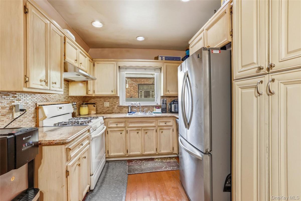 Kitchen featuring light wood cabinetry, a mosaic tile backsplash, a stainless steel refrigerator, and built-in overhead lighting