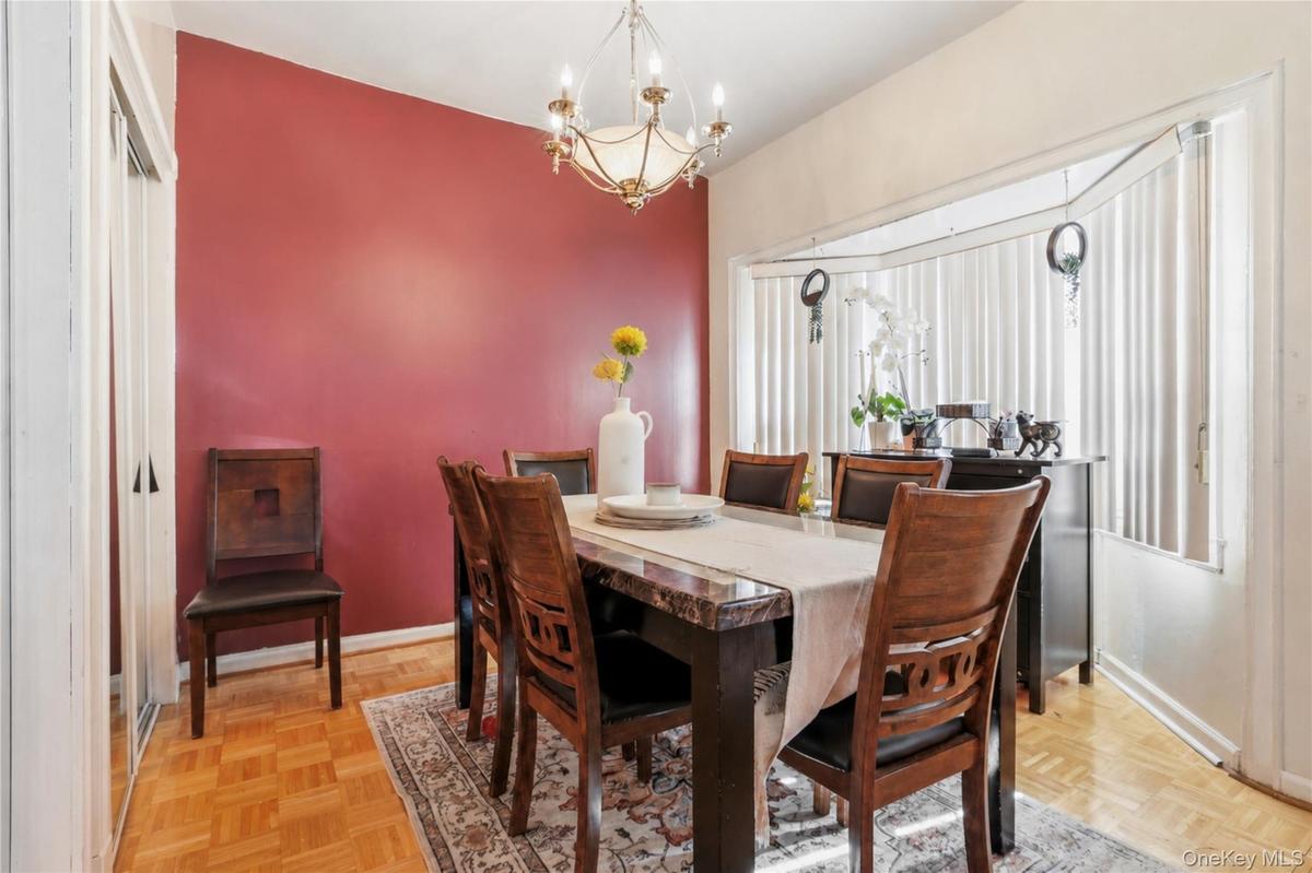 Dining area featuring a prominent red accent wall, parquet wood-finish flooring, and an elegant chandelier
