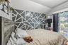 Bedroom featuring a wood-finish headboard, a geometric accent wall, and a window with decorative curtains