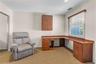 Room featuring a corner wood-finish desk with integrated cabinetry, a window with blinds, a wall-mounted wood-finish cabinet, and textured carpet floo
