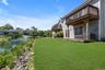Shingle-sided exterior featuring a wooden balcony and ground-level deck, overlooking a manicured lawn and a body of water with a fountain