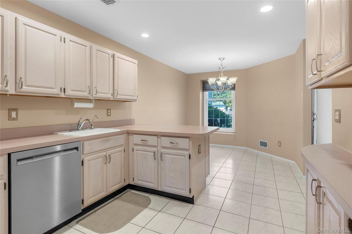Kitchen featuring white cabinetry, light countertops, a stainless steel dishwasher, and white tile flooring