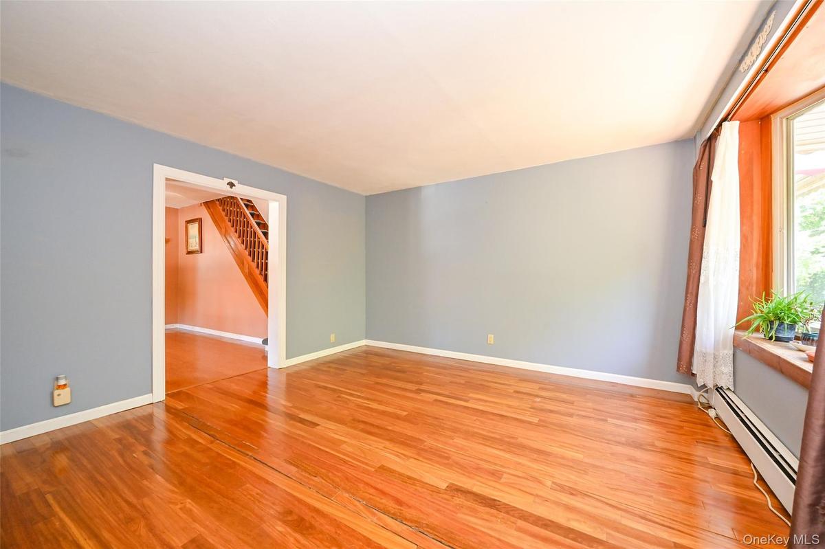Spacious room with Pre-engineered hardwood flooring, light blue wall paint, and a large bay window with wood trim.
