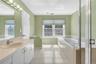Bathroom featuring a built-in tub, separate glass-enclosed shower, dual windows, and a vanity with an integrated sink