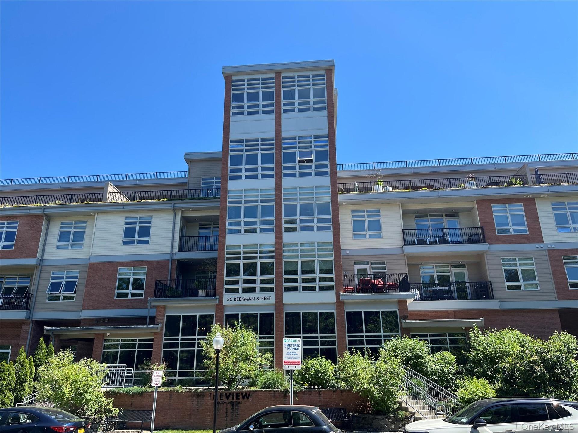 Multi-story residential building featuring a brick and siding exterior, expansive window panels, private balconies with black railings, and a prominen