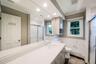 Bathroom featuring a single vanity with an integrated sink, a large wall-mounted mirror, a tiled shower with a sliding glass door, a window with a bli