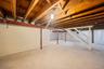 Expansive unfinished basement featuring concrete flooring, exposed wood ceiling joists, and structural support beams