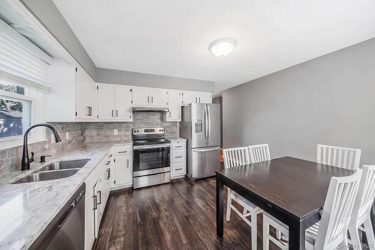 Kitchen featuring white cabinetry, gray subway tile backsplash, light-toned stone-finish countertops, stainless steel appliances, and dark wood-finish