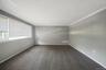 Spacious room featuring neutral gray walls, dark gray carpet flooring, white trim, and a large window with blinds