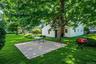 Expansive green lawn with mature shade trees, featuring a square concrete patio and a white exterior home with multiple windows