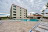 The resort-style pool includes a spacious deck, poolside lounge chairs, and a nearby clubhouse building, all set against a backdrop of palm trees and 