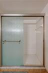 Close-up view of the primary suite’s shower showcases a hexagon tile floor and full tile surround behind frosted sliding doors.