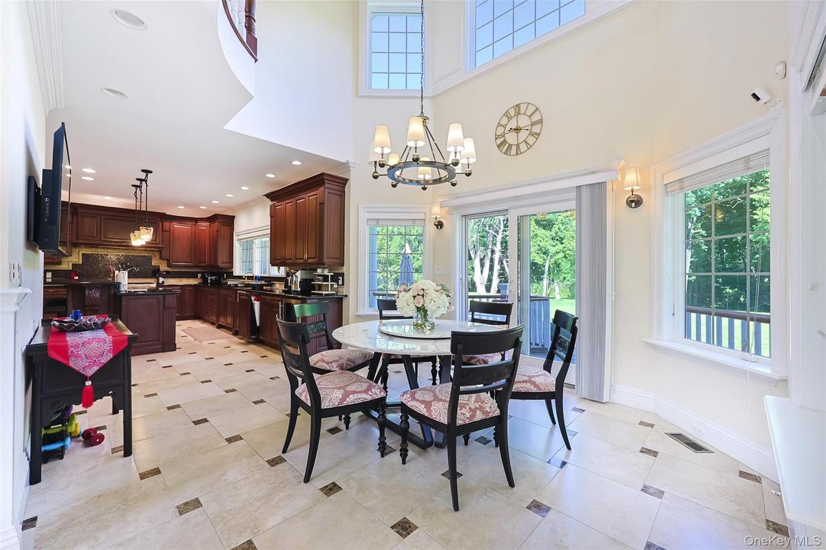 Open-concept kitchen and dining area featuring high ceilings, large windows, tile flooring with decorative inserts, and rich wood cabinetry