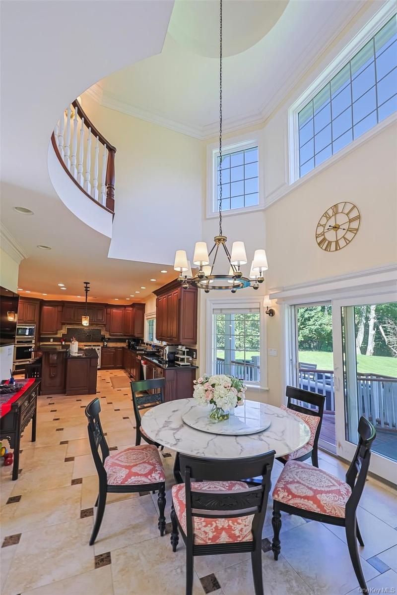 Open-concept kitchen and dining area featuring a two-story ceiling, a circular staircase with white balusters and a dark wood handrail, and high windo