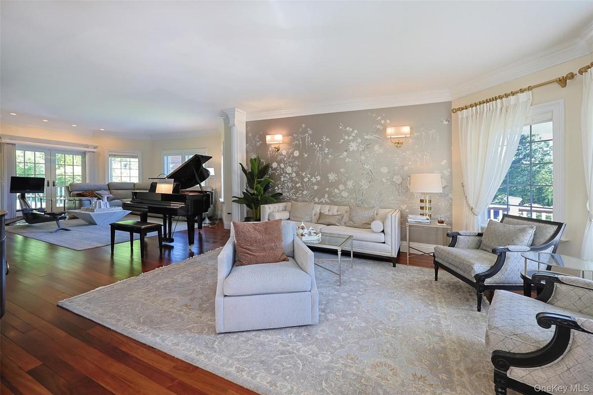 Spacious living area featuring polished wood flooring, a decorative accent wall with sconce lighting, and multiple large windows with white drapery