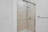 Primary shower with new chrome fixtures, and a handheld shower head, and new glass doors