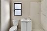 Bathroom featuring a single-pane window, white toilet, vanity with integrated sink, chrome faucet, and large-format porcelain tile shower surround