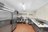 Stainless steel commercial kitchen featuring a large double-door refrigerator, triple basin sink, and ample counter space