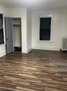Spacious room featuring wood-finish flooring, white baseboards, and a built-in closet with a gray door