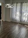 Wood-finish flooring with baseboard trim, contemporary light fixture, and window with sheer patterned curtains