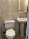 Bathroom featuring floor-to-ceiling ceramic tile, a decorative tile border, pedestal sink with chrome faucet, toilet, and a medicine cabinet with inte