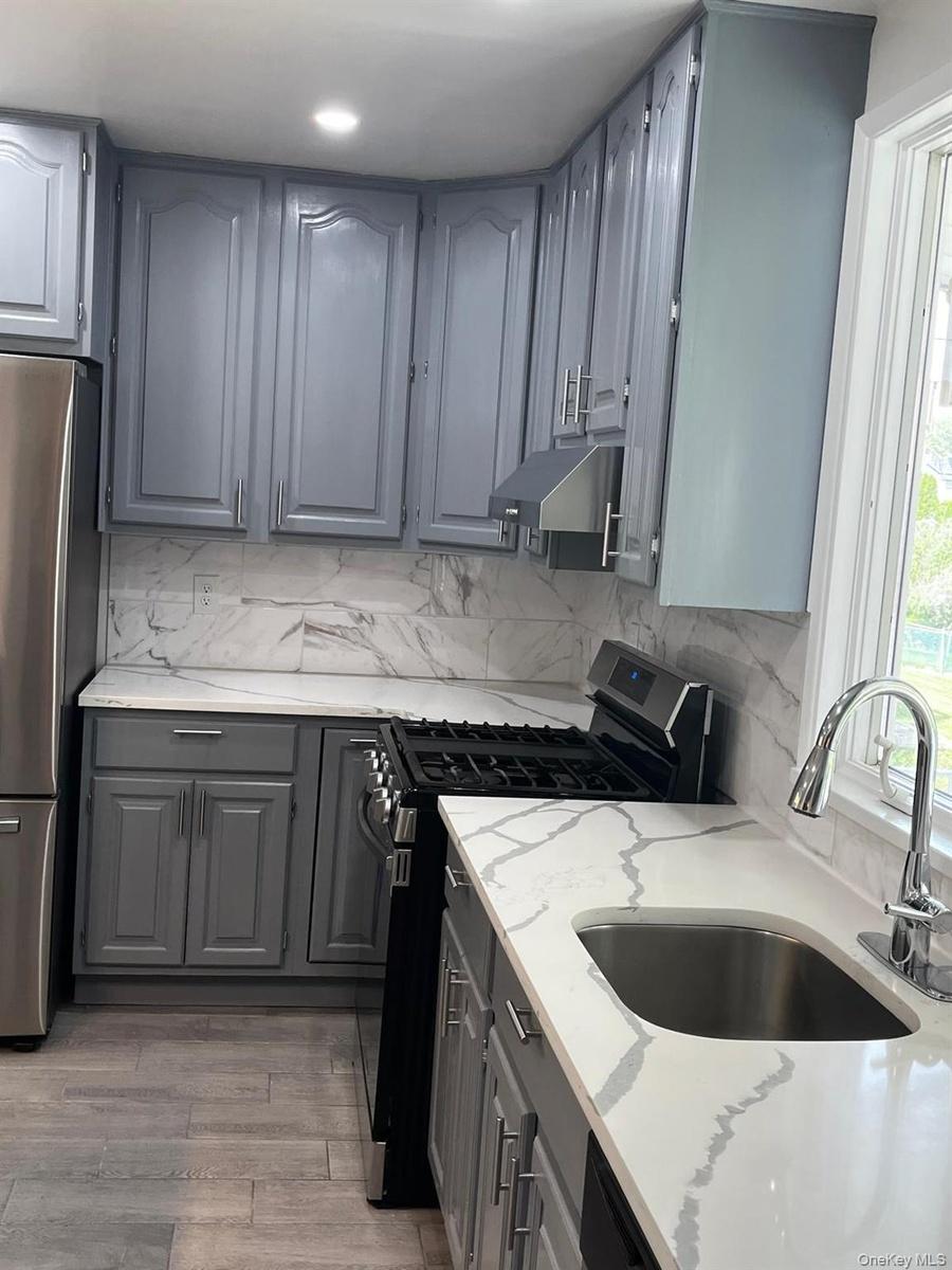 Kitchen featuring grey cabinetry, white countertops with grey veining, a stainless steel sink with a gooseneck faucet, a black range, and wood-finish 