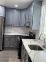 Kitchen featuring grey cabinetry, white countertops with grey veining, a stainless steel sink with a gooseneck faucet, a black range, and wood-finish 