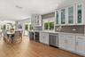 Separate entertaining bar features illuminated cabinetry, a wine refrigerator, sink, second Bosch dishwasher and pass-through window to the lanai