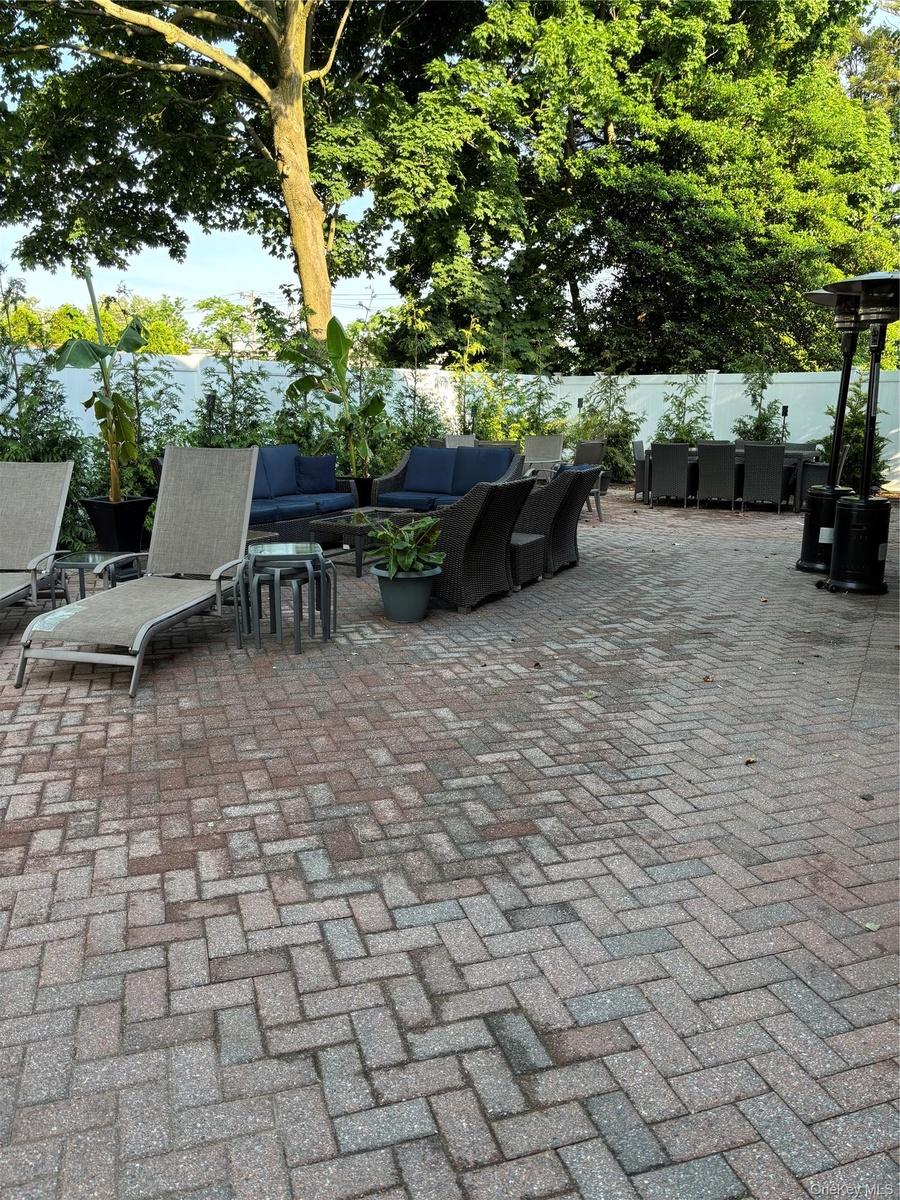 Expansive paver patio featuring a herringbone pattern, mature trees, and a privacy fence