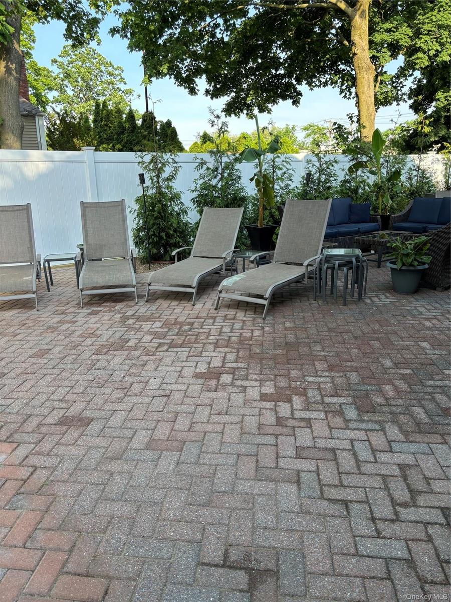 Expansive paver patio with a white privacy fence and mature trees