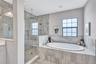 Unwind in a spa-like bathroom featuring a large walk-in shower with a rain shower head, built in bench, and soaking garden tub designed for total rela
