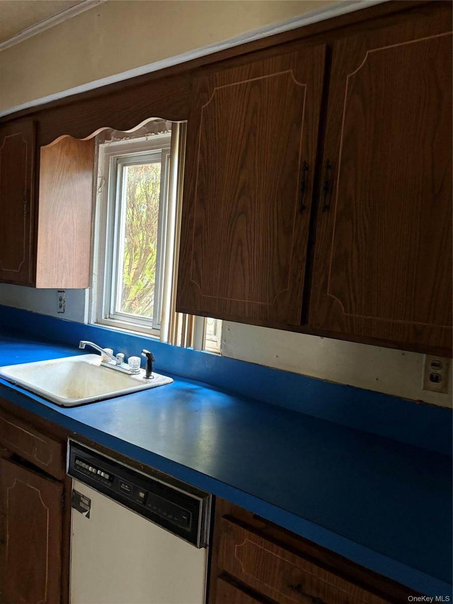 Kitchen area featuring wood-finish cabinetry, a blue countertop, a white drop-in sink with a chrome faucet, and an integrated dishwasher