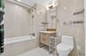 Bathroom featuring full-height light-toned tile, a white bathtub with gold-finish fixtures, a vanity with gold hardware, and a framed mirror with inte