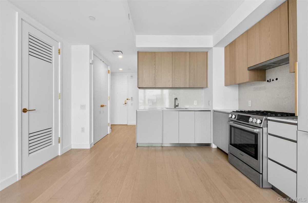 Modern kitchen featuring wood-finish upper cabinetry, white lower cabinetry, and stainless steel appliances