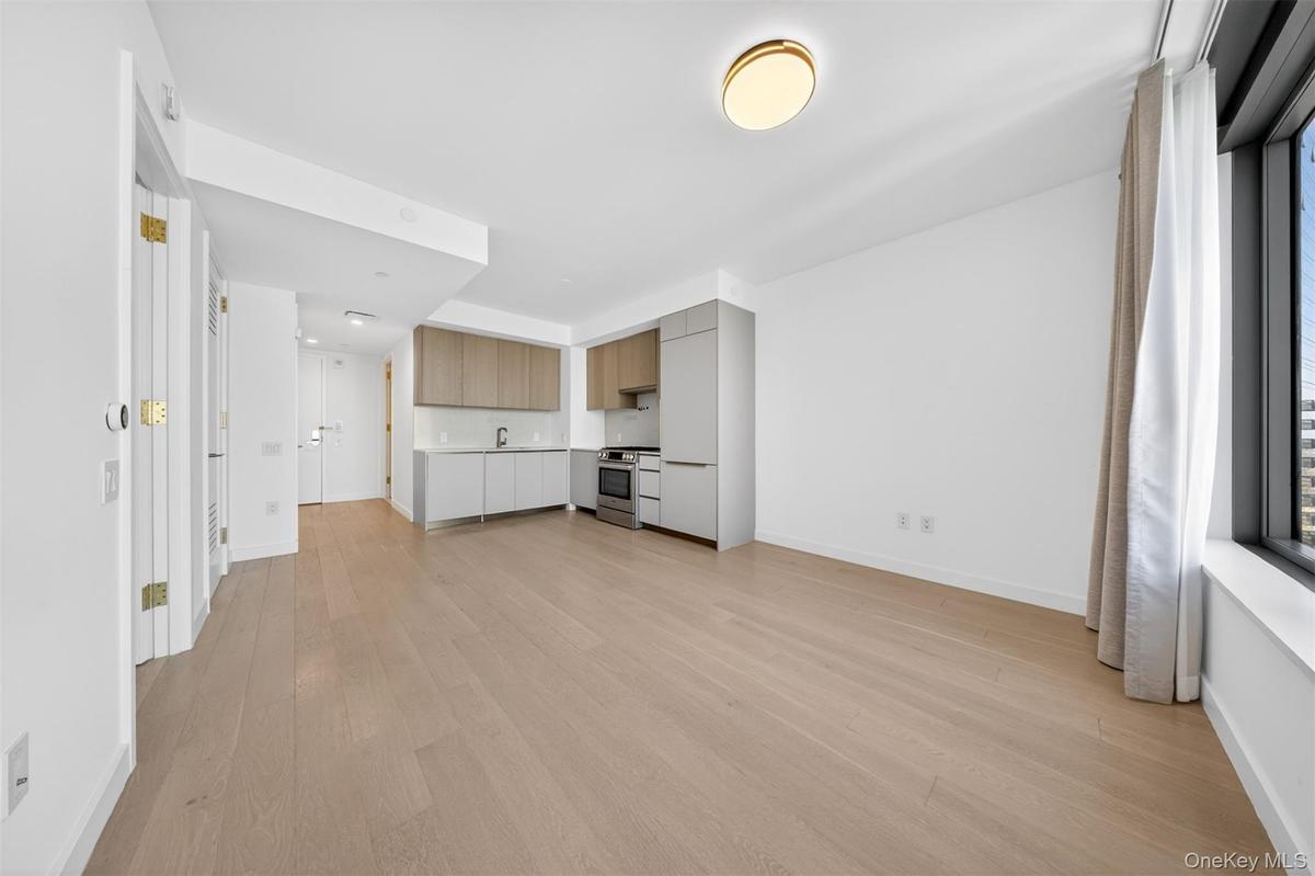 Open-concept living area featuring light wood-finish flooring, a modern kitchen with integrated appliances, upper wood-tone cabinetry, lower grey cabi