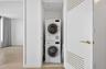 Laundry closet with stacked washer and dryer appliances, featuring a white door with decorative gold-toned detailing and a gold-toned lever handle