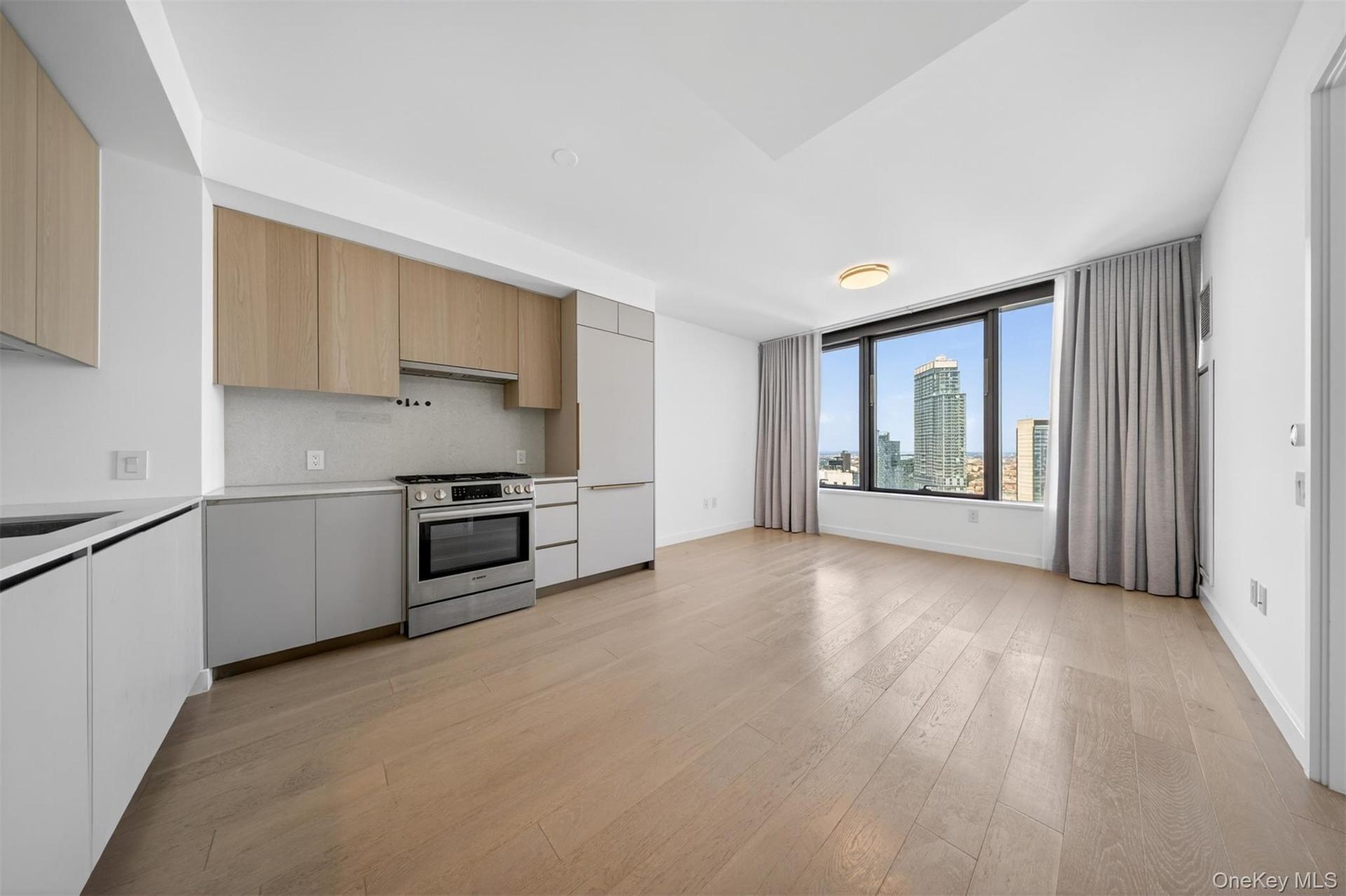 Open-concept living space with wood-finish flooring, a full kitchen, and a large window