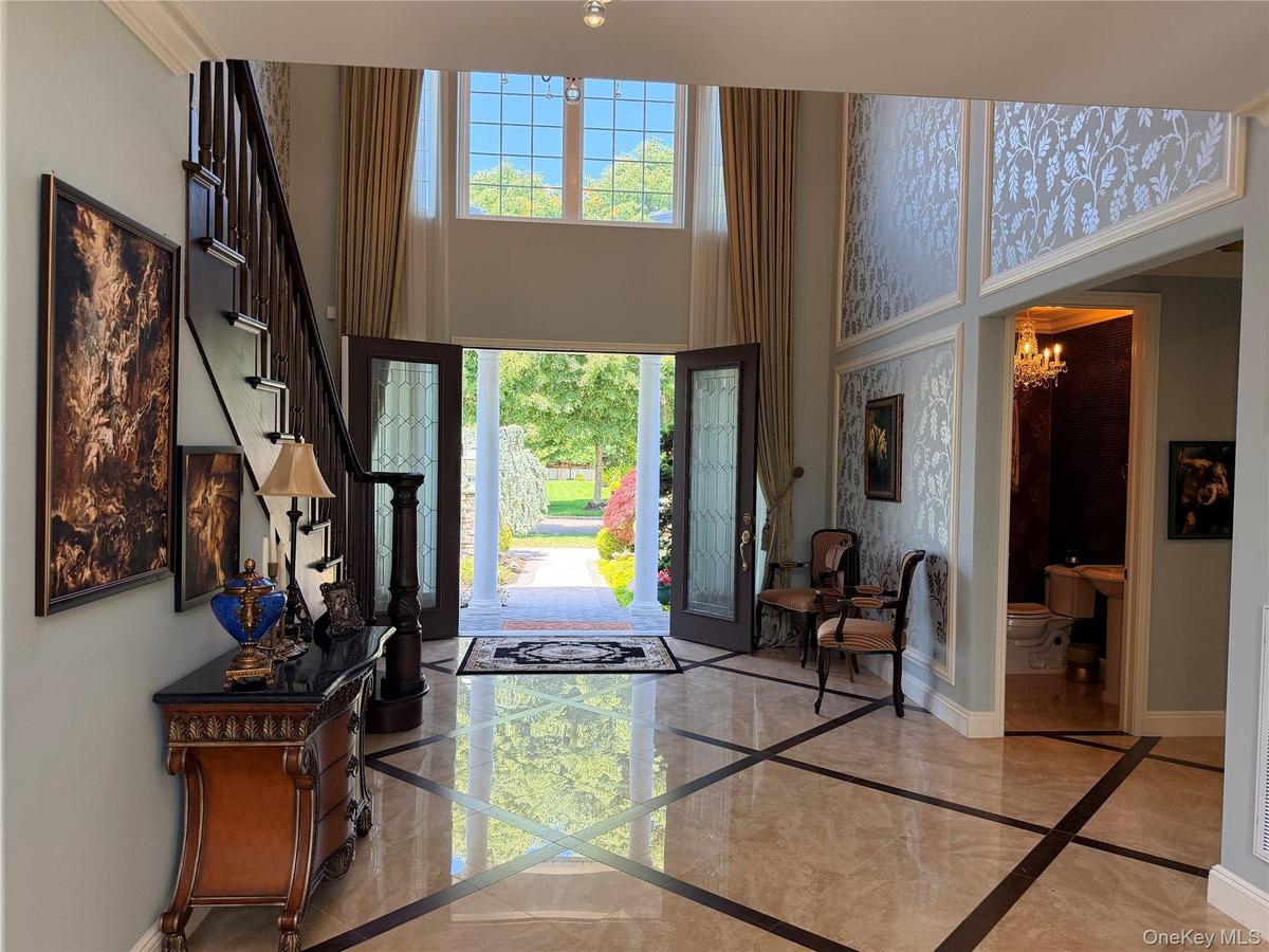 Two-story foyer featuring marble flooring with contrasting inlay, a dark wood staircase with ornate newel post, and decorative wall panels