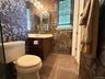 Bathroom featuring patterned wallpaper, a single vanity with a white countertop, a mirror, and a multi-bulb light fixture