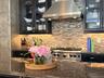 Kitchen featuring dark stone countertops, mosaic tile backsplash, professional-grade gas range, stainless steel range hood, and dark cabinetry with gl