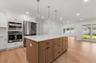 Contemporary kitchen featuring a large central island with a light-toned wood finish, white countertops, built-in stainless steel appliances, and whit